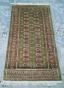 Green ground Persian rug with 28 elephant foot guls arranged across two rows, on a stepped border,