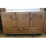 Light elm Ercol sideboard of three cupboard doors above two drawers, the whole raised on castors,