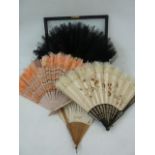 A wooden and silk painted fan with white feather trim, a pink fan with pink feather trim, a black