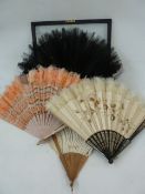 A wooden and silk painted fan with white feather trim, a pink fan with pink feather trim, a black