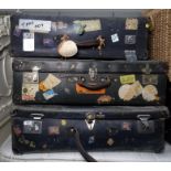 Three large travelling suitcases bearing many travel labels, including British Airport, The