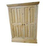 Pine two-door short wardrobe with panelled doors opening to reveal hanging space, raised on