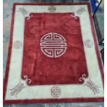 A Chinese wool rug, red ground with central symbol in purple, cream border with symbols and edging