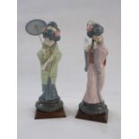 Two Lladro style Geisha figures holding umbrella and fan, one in green kimono, other in purple