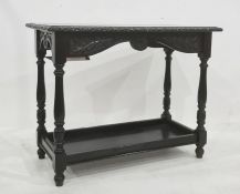 Black painted two-tier table, the rectangular top with carved edge, on turned and block supports
