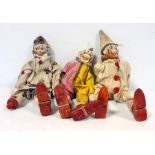 Three early 20th century wooden clown peg dolls with painted faces and in cotton clown costumes,