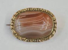 Early Victorian gilt metal broch set with a central cabochon agate within a chased floral border,
