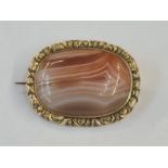 Early Victorian gilt metal broch set with a central cabochon agate within a chased floral border,