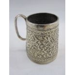 Indian white metal mug of tapering cylindrical design, the body decorated with scrolling foliage and