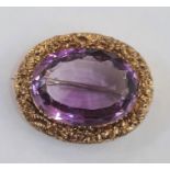 Gold brooch set with a central oval mix cut amethyst and surrounded by a chased floral border, 3cm