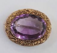 Gold brooch set with a central oval mix cut amethyst and surrounded by a chased floral border, 3cm