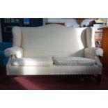 A Georgian style mahogany wingback sofa,cream upholstery, on reeded legs joined by stretchers,