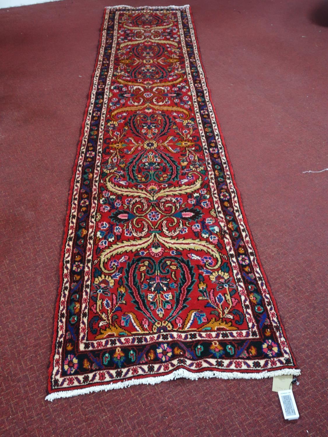 A Northwest Persian Sarouk runner, repeating stylised floral motifs on a rouge field, complimented