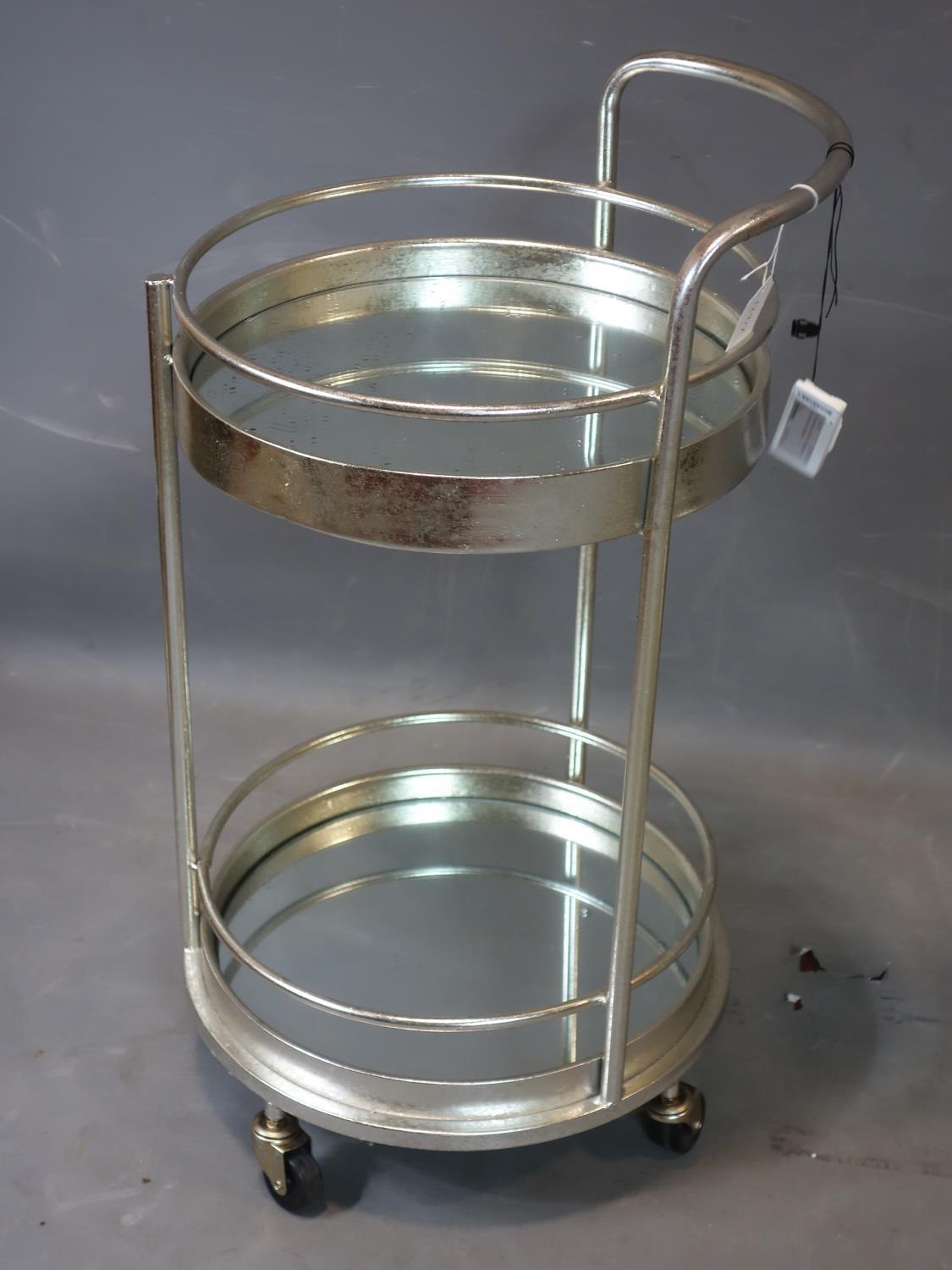 A contemporary silver painted circular two tier drinks trolley, with mirrored tops, raised on