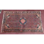 A Persian rug with central diamond medallion and floral motifs on a rouge ground, within floral