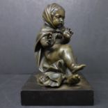 A bronze figure of a baby girl in cloak sitting on a cushion, rubbed signature to reverse, on marble