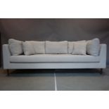 A contemporary three seater sofa with grey linen upholstery, raised on tapered teak legs