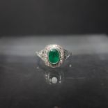An Art Deco style platinum ring, set with central emerald surrounded by diamonds, size O