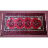 A North East Persian Meshad Belouch rug, repeating stylised medallion on a rouge field within