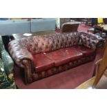 A Chesterfield button back red leather sofa, on bun feet, with associated cushions, H.72 W.240 D.