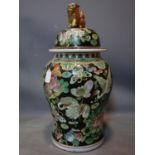 A large early 20th century Chinese temple jar and cover, with flora and fauna decoration, on a black