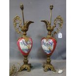 A pair of Italian brass and porcelain lamps in the form of ewers, with scrolling handle, decorated