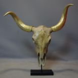A faux bison skull with gilt painted horns, on stand, H.72 W.78cm