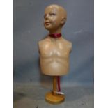 An early 20th century painted fibreglass mannequin of a child, raised on wooded stand, H.65cm