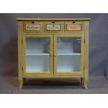 A French distressed painted side cabinet with three drawers above a pair of glazed panel doors, on