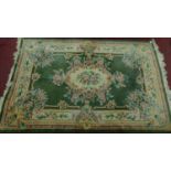 A large ornate Chinese rug with emerald central floral design on a green ground and cream border.