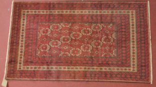 A Persian meshad belouch rug, repeating stylised geometric motifs on a red field within multi