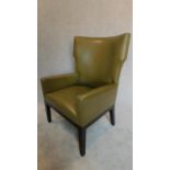 A contemporary designer green leather wing back armchair, raised on ebonized legs, with makers stamp