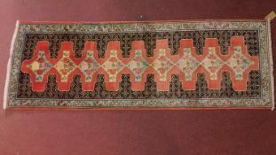 A north west Persian Senneh runner, repeating stylised diamond medallions on a rouge field.