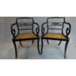 A pair of Regency ebonized scroll armchairs, with caned seats and gilt metal mounts, raised on sabre