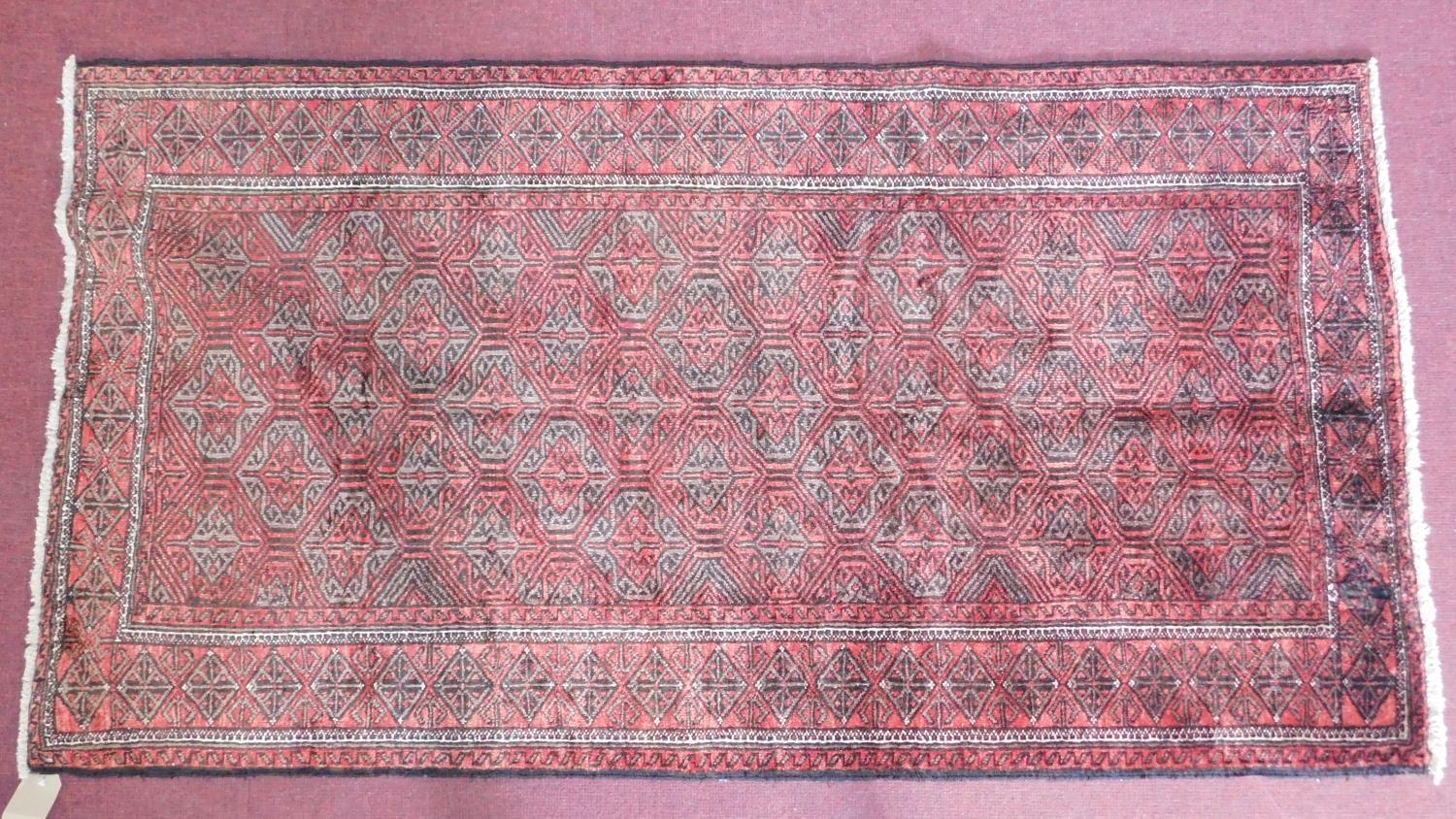 A north east Persian Hatchlie carpet with repeating stylised geometric motifs on a rouge field