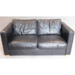 A contemporary two seater black leather sofa on block feet. 68x102x90cm