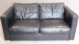 A contemporary two seater black leather sofa on block feet. 68x102x90cm