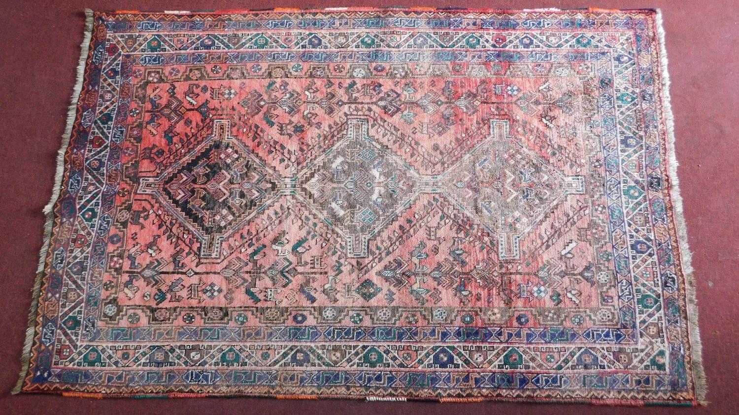 A Persian Qashqai rug with triple pole medallion and repeating geometric motifs on a terracotta