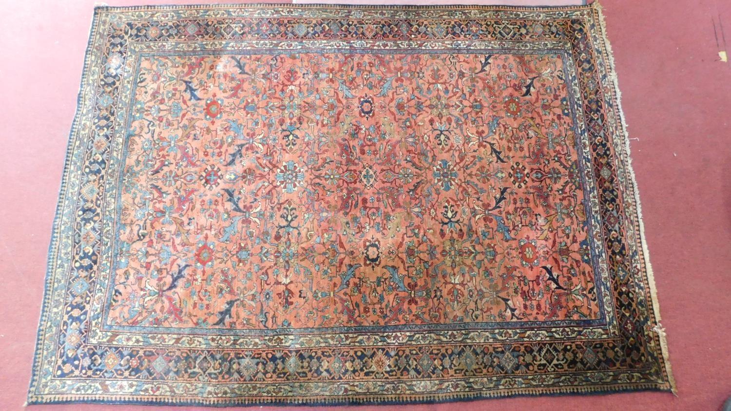 A large Persian rug with repeat motifs on a rouge back ground surrounded by a stylised floral and