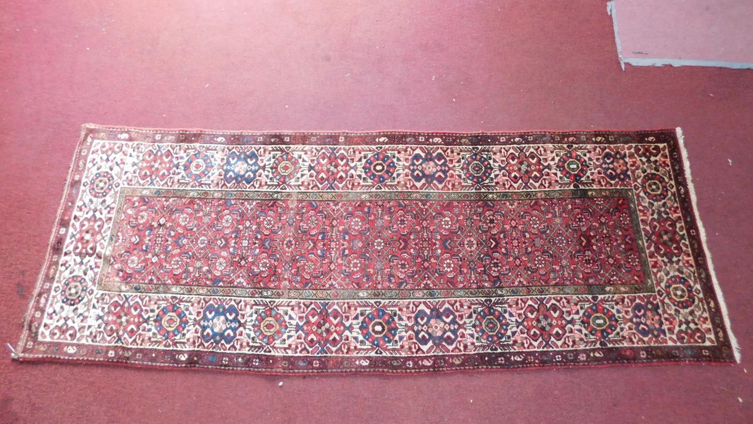 A Persian Heriz style runner, repeating stylised gul motifs on a terracotta field, within