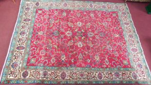 A large Kashan style rug with repeat motifs on a rouge floral back ground surrounded by a stylised