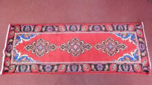 A Persian rug, red triple pendant medallions on a rouge ground, within floral borders, fringed