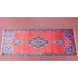 A Persian rug, red triple pendant medallions on a red ground, within geometric borders,