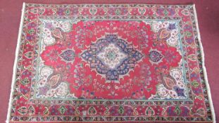 a large Persian rug, with a central double pendant medallion, on a rouge field with repeating floral