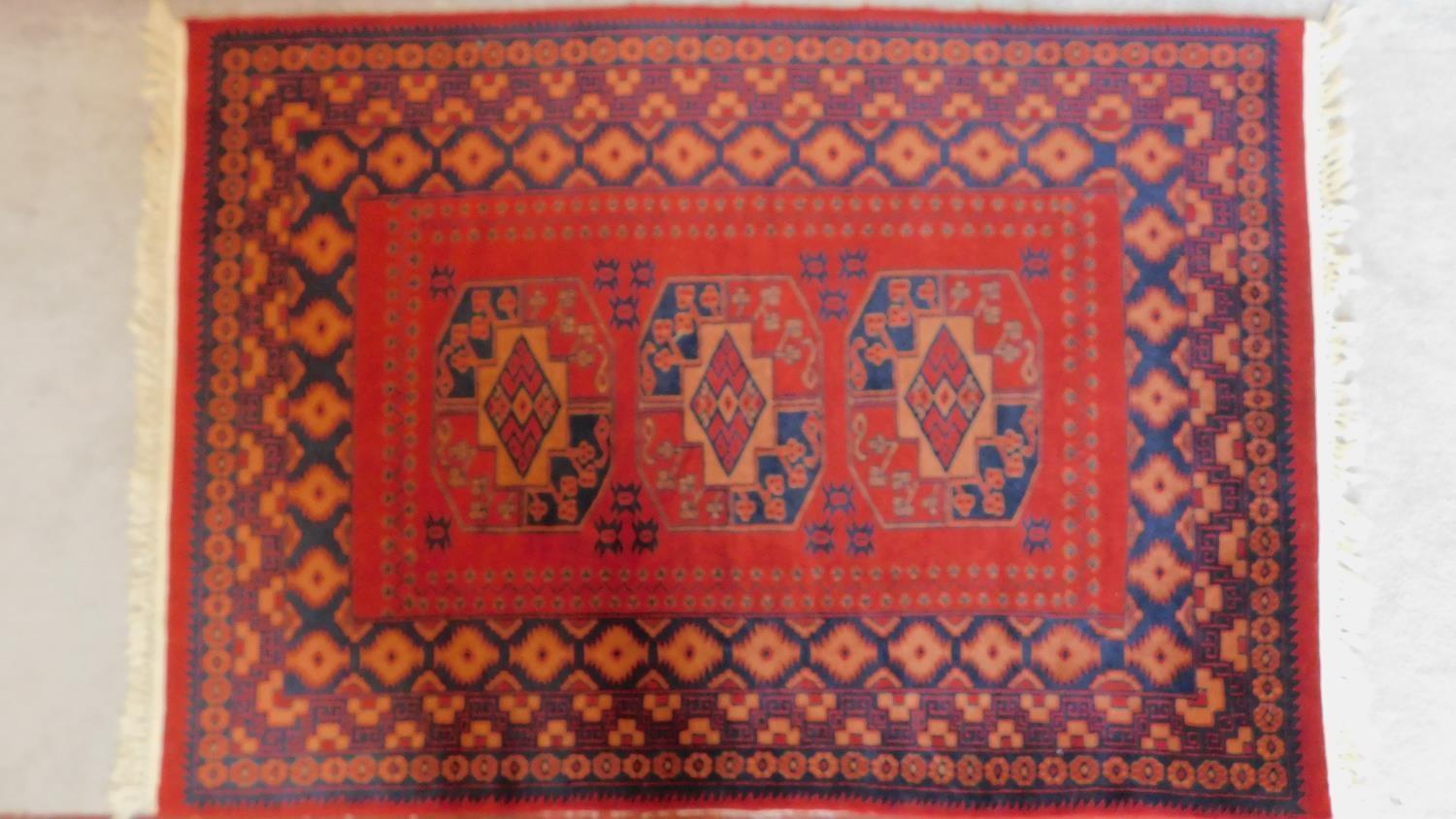 A Persian style rug with triple pendant medallions on a terracotta field surrounded by repeating