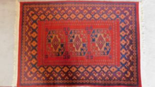 A Persian style rug with triple pendant medallions on a terracotta field surrounded by repeating