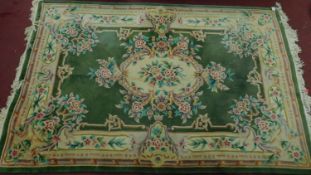 A large ornate Chinese rug with emerald central floral design on a green ground and cream border.
