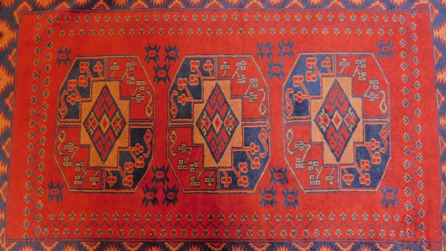 A Persian style rug with triple pendant medallions on a terracotta field surrounded by repeating - Image 4 of 4
