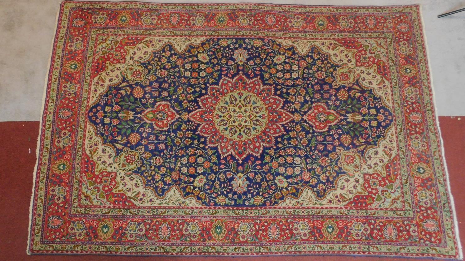 A Tabriz rug with central medallion and repeating floral motifs set on a predominantely rouge and
