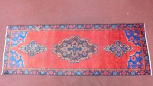 A Persian rug, red triple pendant medallions on a red ground, within geometric borders,